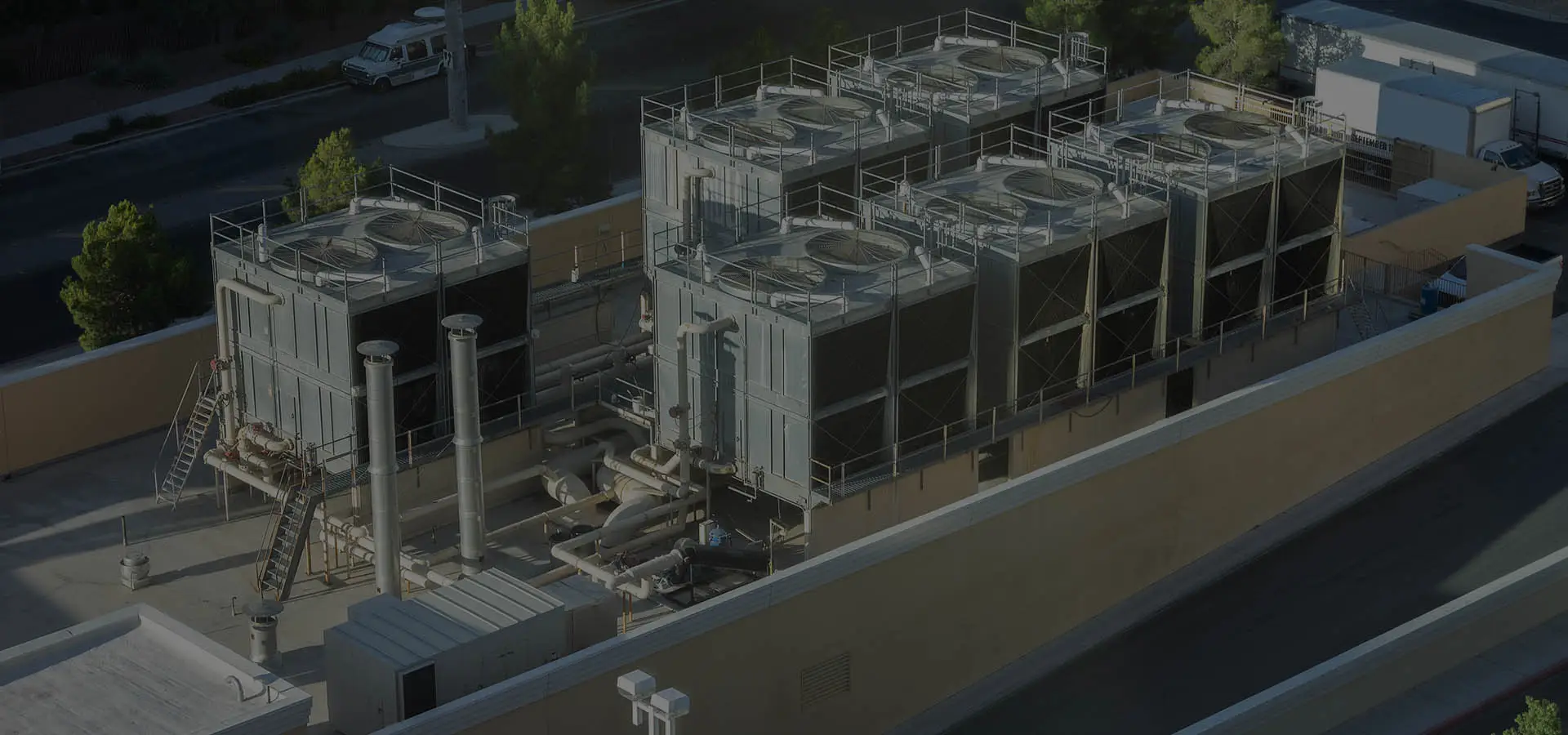 Large industrial HVAC cooling towers with multiple fans and piping on a commercial rooftop facility.